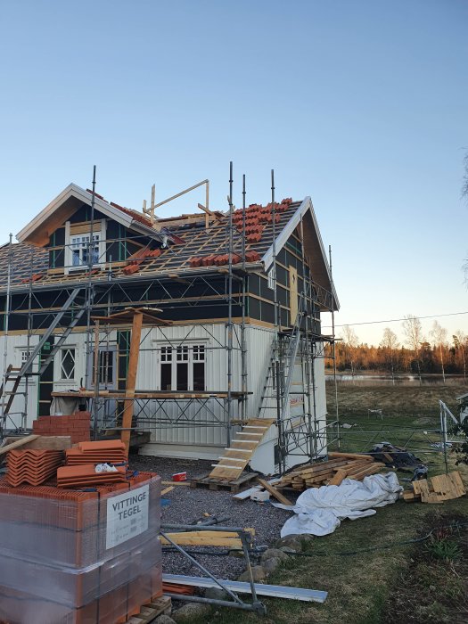 Under konstruktion hus med hål i taket täckt för skorstensinstallation, plattform och byggmaterial runtomkring.