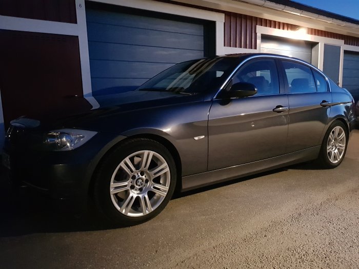 Välpolerad grå BMW parkerad framför en garageport under skymningen.