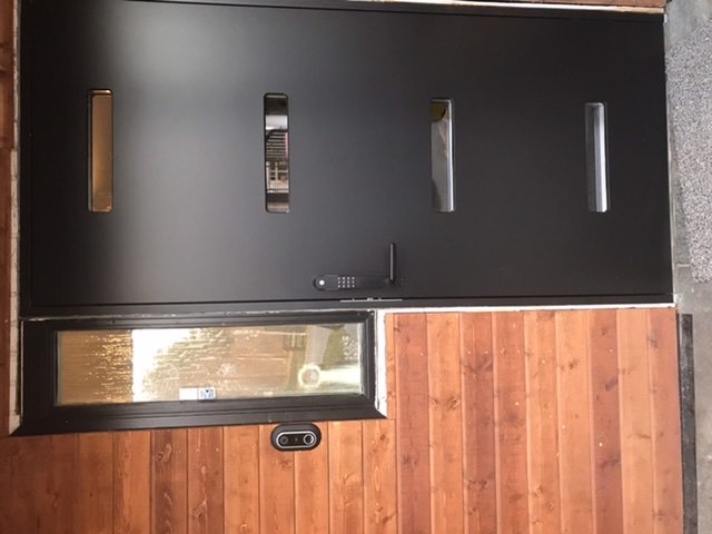 Sned bild av svart dörr med lasyreffekt och trävägg, sett inifrån ett hem.