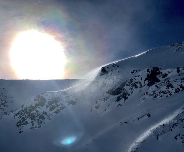 Sol som skiner över ett snöklätt bergslandskap med ljusreflex och linsflare.