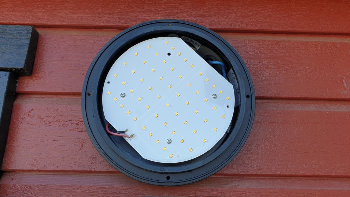 LED-panel för utomhusbelysning monterad på en röd vägg, synlig driverelektronik.