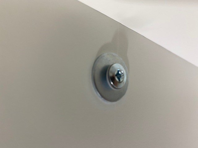 En metallspikplugg monterad på en vit vägg, som håller fast en kloss eller platta.