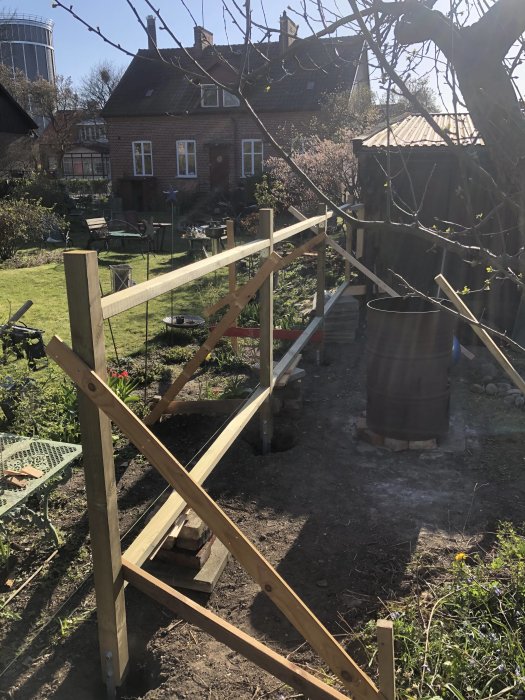 Stomme av nytt träplank under uppbyggnad i solig trädgård med hus i bakgrunden.