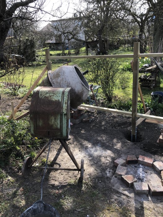 Gammal betongblandare och nygjorda plinthål i en vårig trädgård som förebådar kommande byggprojekt.