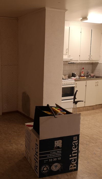 Pudset skorsten i køkken med hvid maling og et repareret område nederst. Der er en papkasse foran og køkkenskabe i baggrunden.