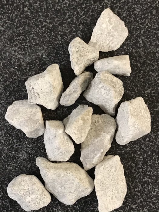 En hög med vit kvartsitstenar i storlek 8-11mm på en granitbänk, som visar kontrasten mellan nyare ljusa och äldre mörkare stenar.