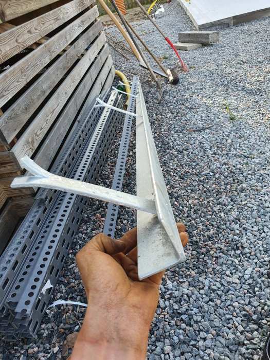 Hand som justerar ett metallbeslag nära staplar av kantelement på grus underlag.