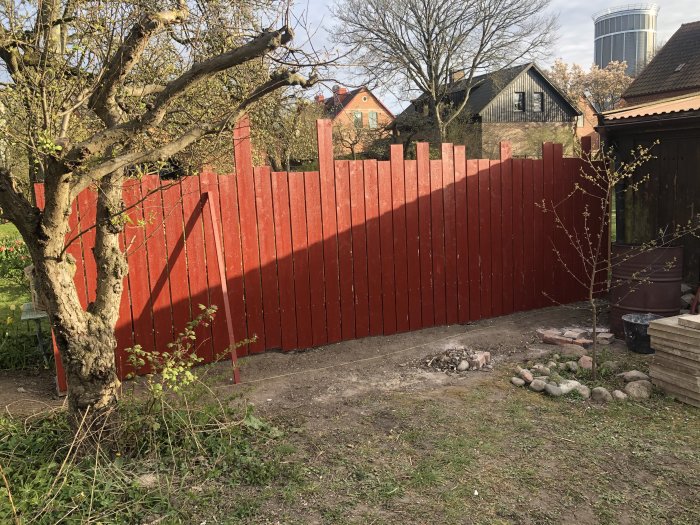 Nyuppbyggt rött plank i trädgården, stolpar synliga, med brädor staplade i förgrunden.