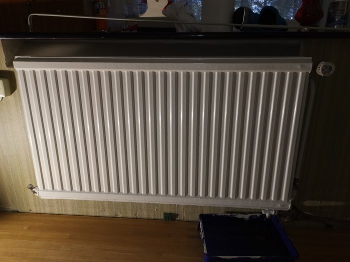 Vit radiator med tappad urtappningskran och målarform under för att samla upp vatten.