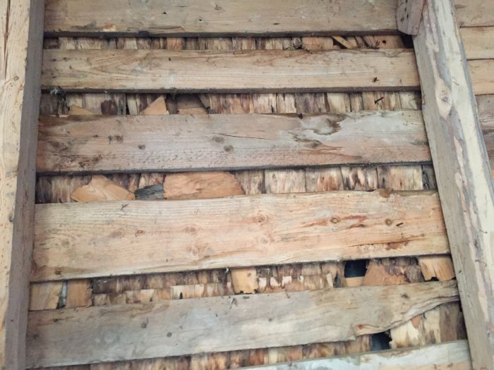 Slitet trägolv eller tak med synliga skador och sprickor i en äldre byggnad.