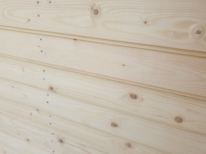 Ny spikad träfasad med tjärbehandling på en stuga, visar träets textur och spikdetaljer.