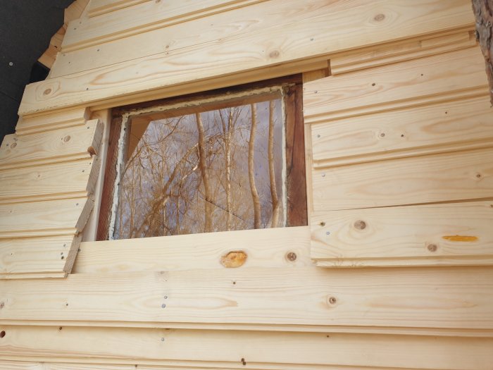 Ny fasadbeklädnad av trä med ett återanvänt gammalt fönster i en stuga.