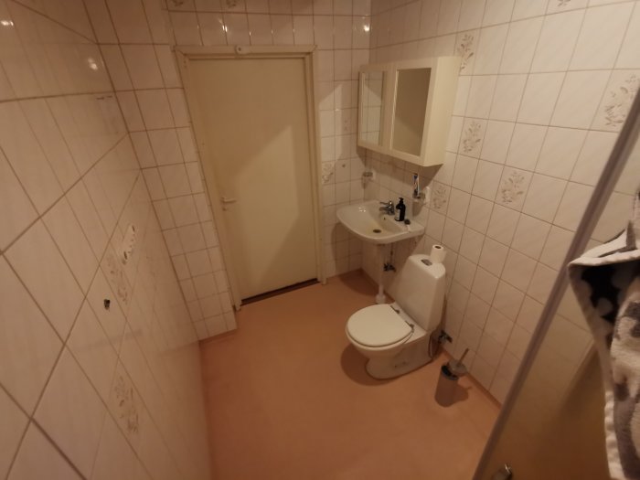 Gammalt kaklat badrum redo för renovering med toalett, handfat och duschhörn.