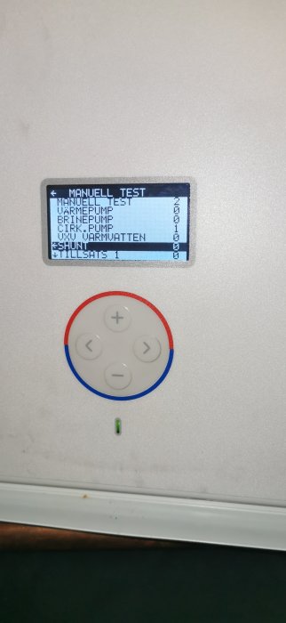 Värmesystemets kontrollenhet med display som visar "MANUELL TEST" och knappsats.