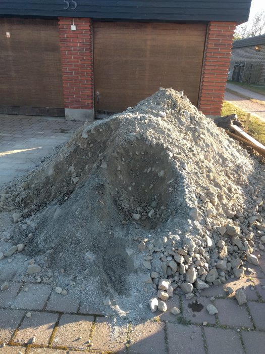 Hög med olika stenar och grus framför en garageport, bredvid en grop i marken.