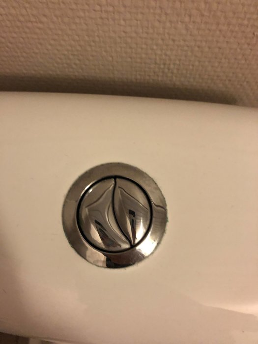 Toalett med närbild på spolknapp utan synligt märke för identifiering.