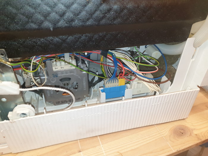 Interiör av maskin med öppen panel som visar sladdar, slangar och mekaniska komponenter under underhåll.