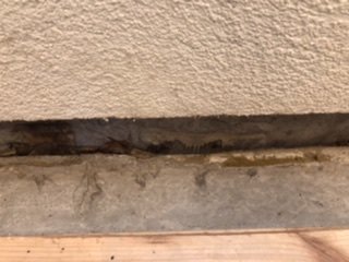 Närbild av en glipa mellan en vägg med grov struktur och ett trägolv som kan indikera ett behov av reparation.