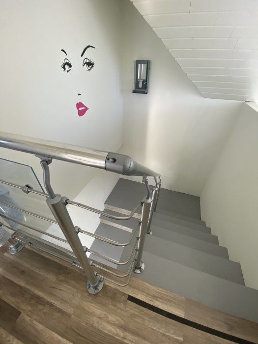 Trappa med metallräcke och 90 graders rörböj, vit vägg med dekorativ målning av ansikte.