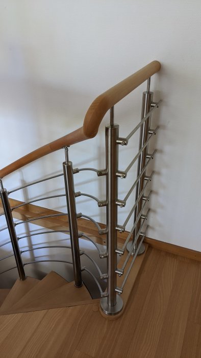 Modern trappa med rostfritt stålräcke, trähandtag och kabelsystem mot vit vägg.