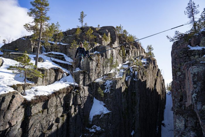 Person som traverserar en snöklädd bergsklöva med säkerhetslina.