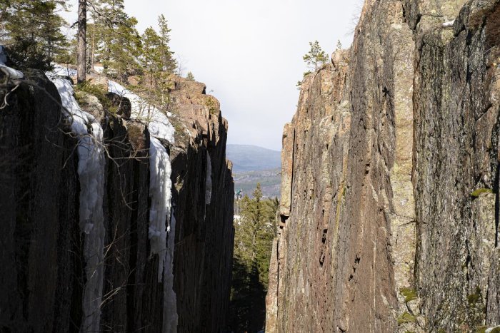 Klyfta mellan höga klippväggar med istappar under en solig dag.
