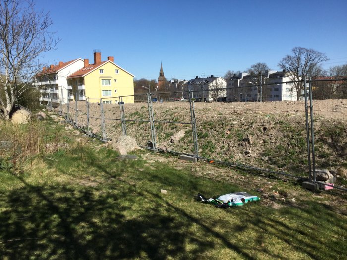 Tomt med avsågade träd och stängsel, berggrund och gräsmatta i ett bostadsområde.