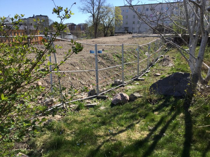 En tomtröjning med synliga berg och jord, gräsmatta till höger och ett tillfälligt staket som markerar en ny tomtgräns.