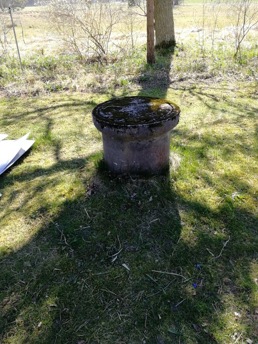 Altanprojekt: En gammal rund brunn av betong på en gräsmatta, omgiven av natur.