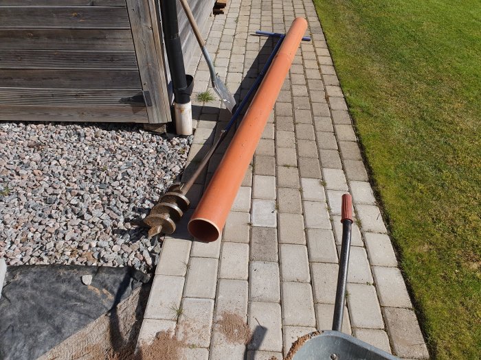 Jordborr och brunnsrör på stenlagd uteplats, redo för projekt med brunnsborrning.