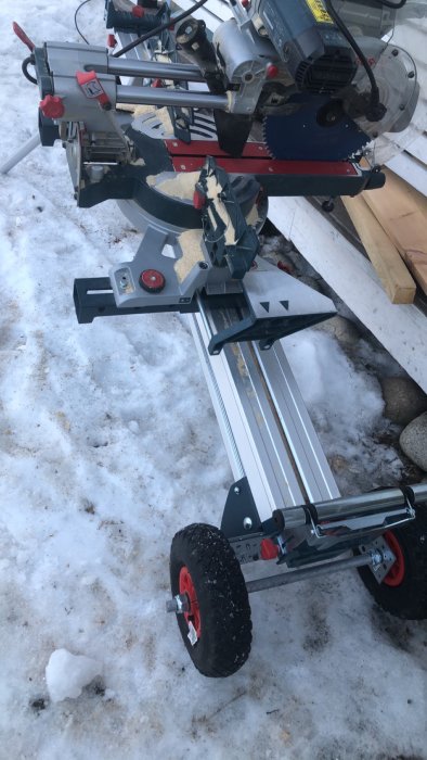 Hemmagjord vagn med röda hjul för en kapsåg på snötäckt mark, byggd med vinkeljärn och en gängstång.