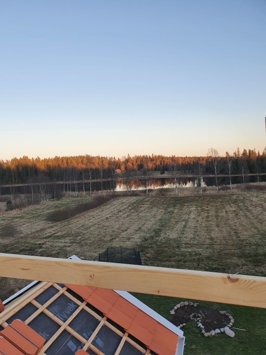 Nybyggd träplattform med extra stag och strävor, med utsikt över en äng och skog vid solnedgången.