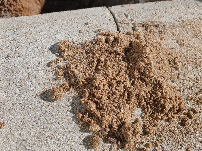 En hög av finkornig, torr sand på en betongyta som visar olika sandfraktioner.