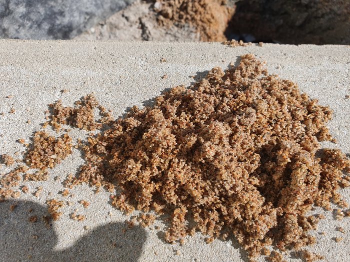 En hög med finsand på betong med skugga, representerar olika sandlager vid borrning.