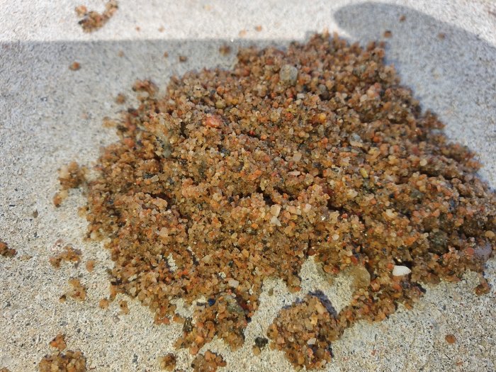 Närbild på en hög med blöt, grov sand med småsten i varierande nyanser av brunt.