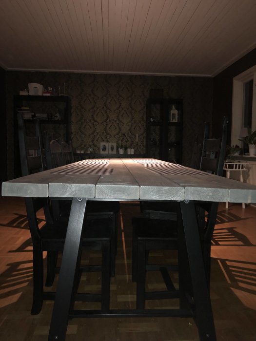 Sex icke limmade, skruvade träbrädor utgör det rustika bordets topp i ett mörkt rum.