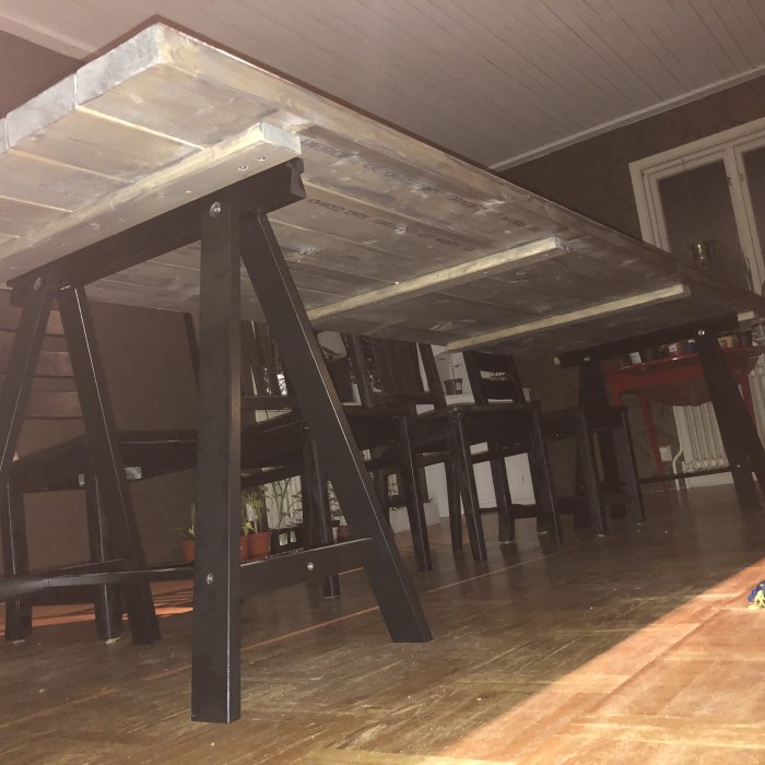 Undersida av handgjord bordsskiva av ihopskruvade brädor och mörka bordsben i ett rum.