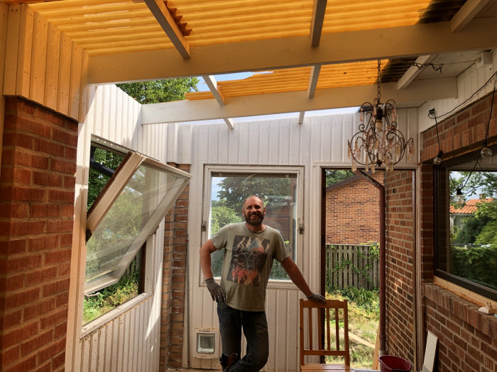 Person i uterum med nytt gult plasttak och verktyg, vindöppet fönster och byggmaterial runtomkring.
