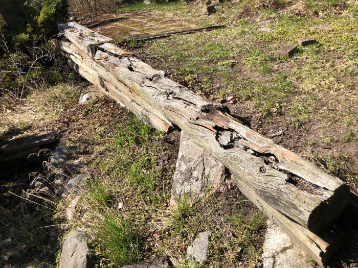 Söndervittrad gammal slipers som använts som stödmur i en trädgård, med synligt slitage och förfall i naturlig miljö.