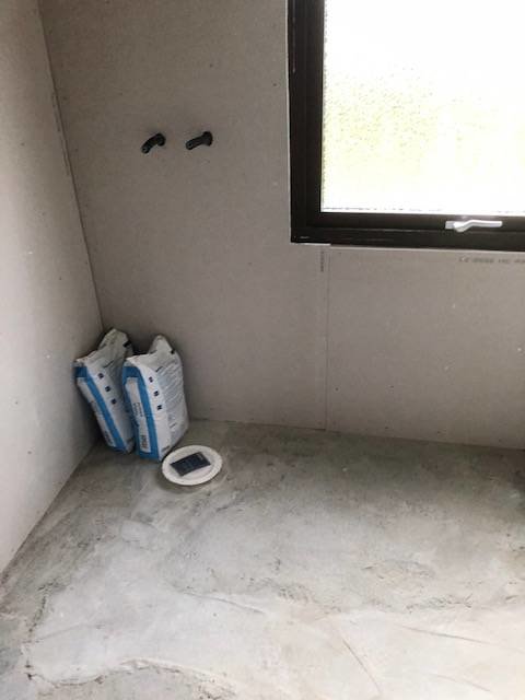 Renoveringsprojekt av badrum med synliga rörgenomföringar och en golvbrunn på vit kakel.