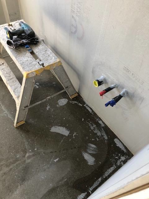Delvis renoverat badrum med osatta kakelplattor, rörutgångar på vägg och en arbetsbänk med verktyg.