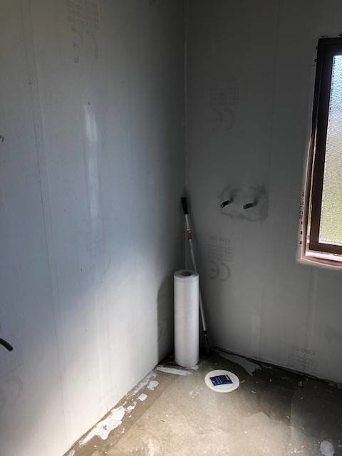 Pågående badrumsrenovering med oskyddade rörledningar och elinstallationer på en vägg nära ett fönster.