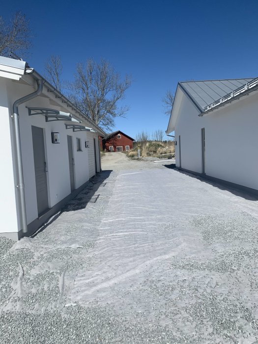 Nygrusad gångväg mellan vitmålade byggnader med en person som lutar sig mot en vägg.