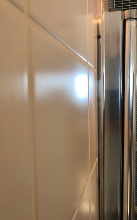 Duschvägg som lossnat vid övre infästningen med synbar böjning och skugga på kakel.