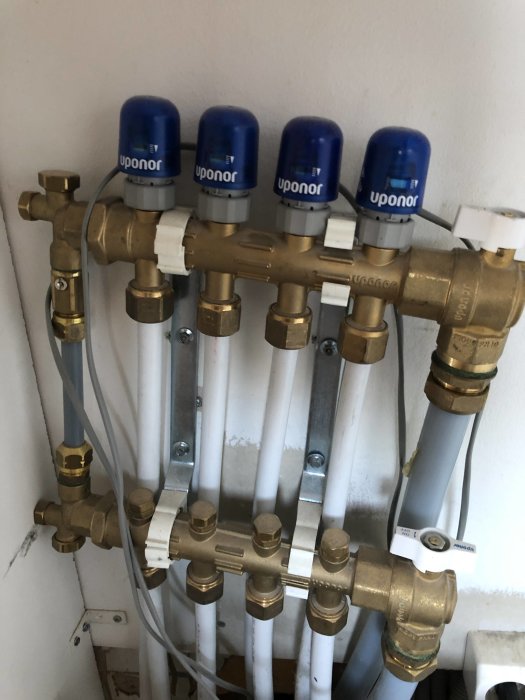 Fördelare för golvvärme med flera anslutna slingor och blå ventilkåpor märkta med Uponor.