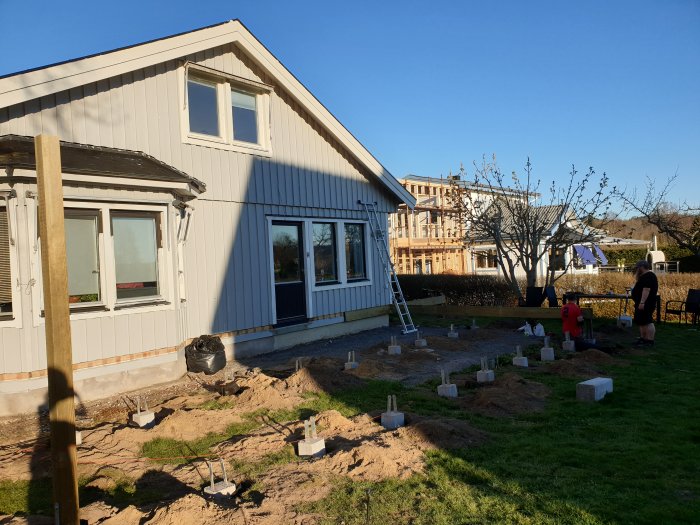 Early construction stage of an altan with foundation plinths and posts next to a house.