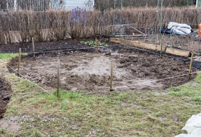 Grävd cirkel i trädgård med sand, markerad med snören och planbräda synlig, redo för stensättning.