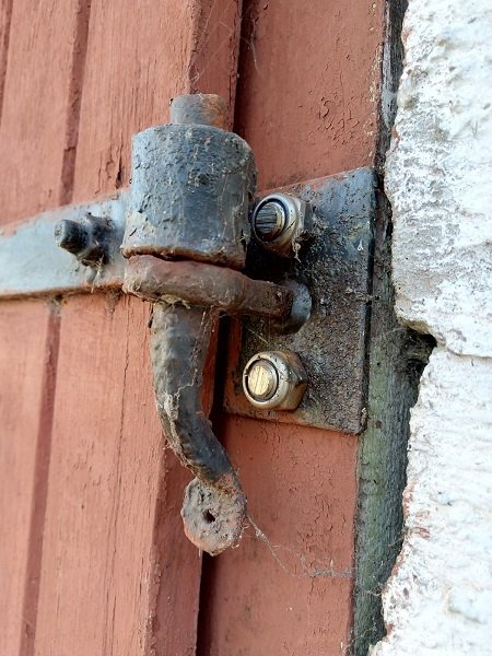 Ett klassiskt hakgångjärn monterat på en röd stolpe med grovt tillhuggen grop och gängade muttrar.