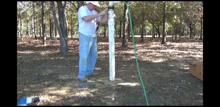 Person som installerar ett rör för brunnborrning utomhus med verktyg och vatten som cirkulerar.