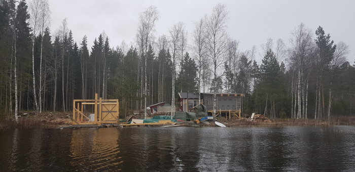 Byggplats vid sjökant med pågående utbyggnad av båthus och presenningar över material.